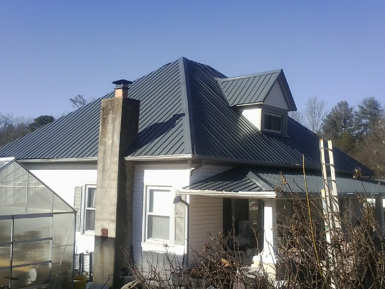 Dark blue standing seam metal roof on a white farmhouse with dormer — Slate & Tile Roof Repair by Roofing Brothers in Fort Myer