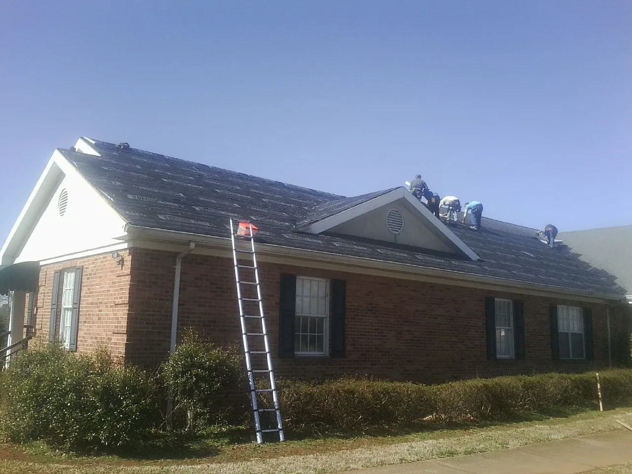 Crew tearing shingles off a brick ranch roof with a ladder set — Metal Roof Repair work by our crew in Fort Myer