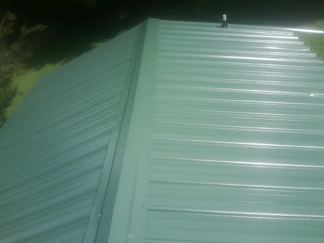 New green metal panels meeting at the ridge of a roof — Flat Roof Repair work by our crew in Fort Myer