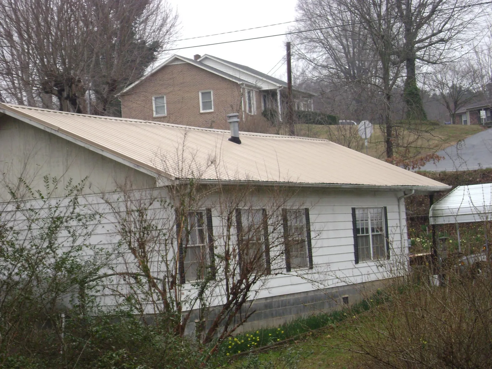 Tan metal roof on a white sided house set into a hillside — Commercial Roofing by Roofing Brothers in Fort Myer
